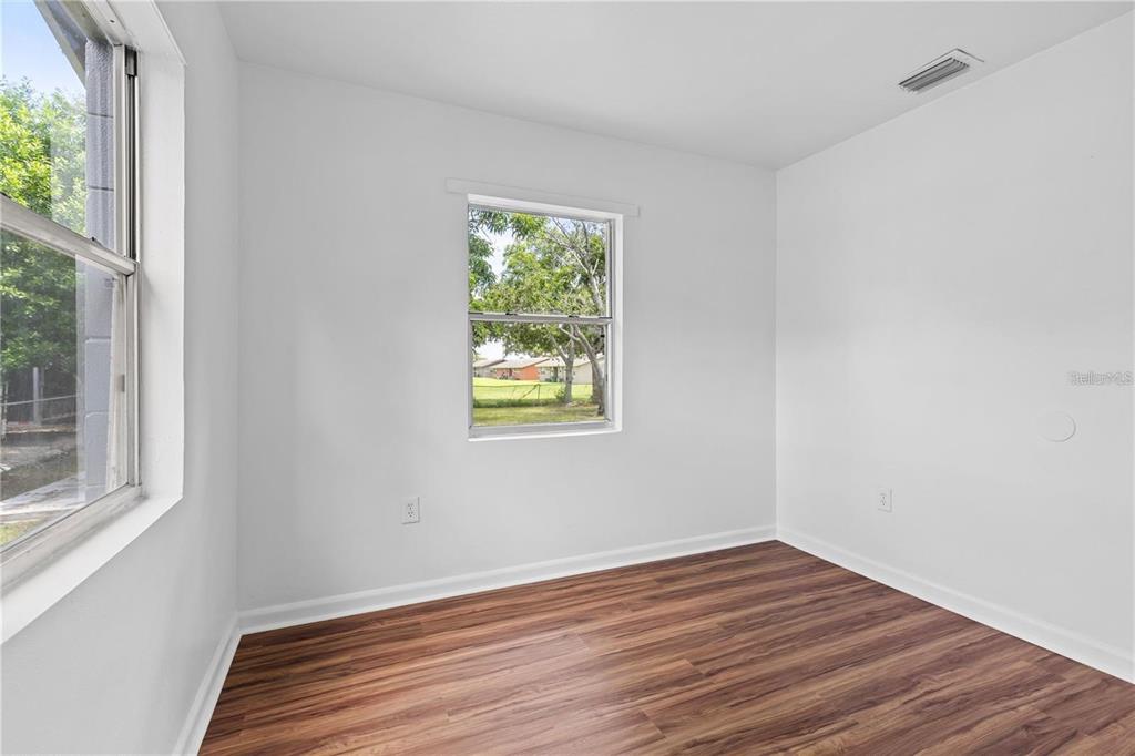 An empty room with white walls, wood-look flooring, and two windows overlooking a yard — 2314 N OSPREY AVENUE, SARASOTA, FL