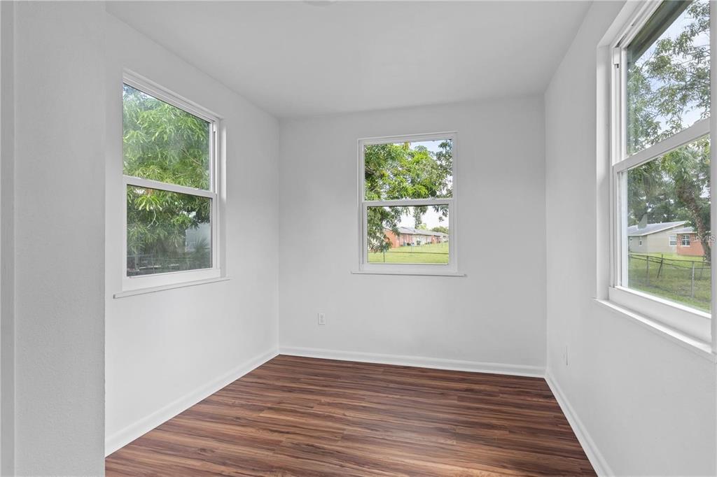 An empty room with white walls, wood-look flooring, and three windows overlooking a yard — 2314 N OSPREY AVENUE, SARASOTA, FL
