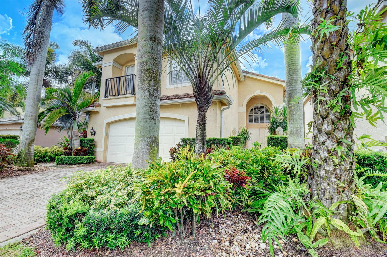 A two-story stucco house with a two-car garage, a balcony, and lush tropical landscaping — 8957 Sandy Crest Lane, Boynton Beach FL 33473, BOYNTON BEACH, FL