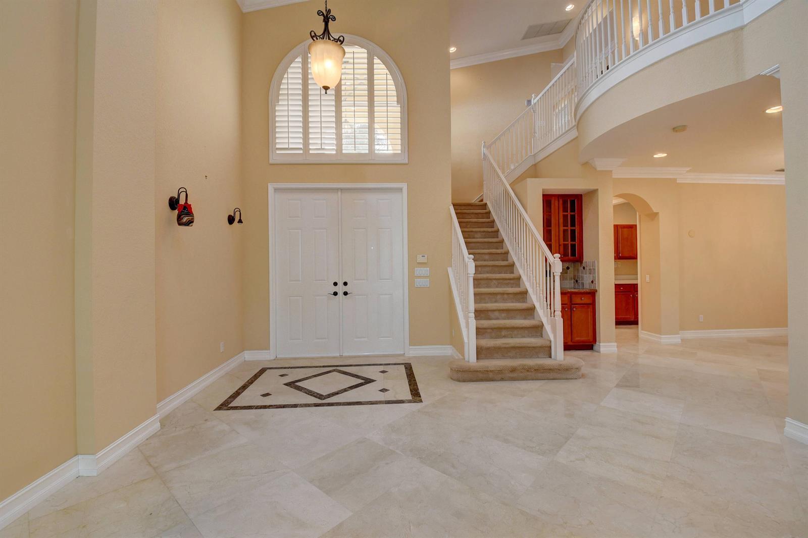 A grand foyer features a double front door, a curved staircase, and light-colored tile flooring — 8957 Sandy Crest Lane, Boynton Beach FL 33473, BOYNTON BEACH, FL