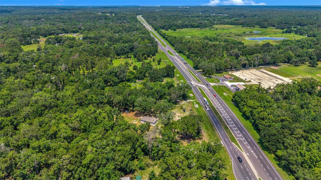 An aerial view shows a house surrounded by dense forest next to a divided highway — 24050 CORTEZ BOULEVARD, BROOKSVILLE, FL