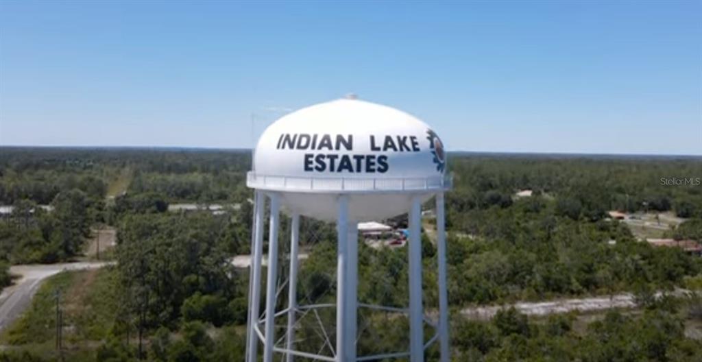 An aerial view shows a white water tower labeled Indian Lake Estates above wooded land — 220 MAGNOLIA DRIVE, INDIAN LAKE ESTATES, FL