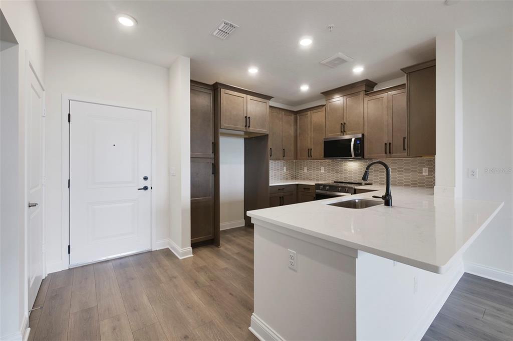 A modern kitchen features dark wood cabinets, a white quartz island, and light wood flooring — 7545 LAUREATE BOULEVARD UNIT 7404, ORLANDO, FL