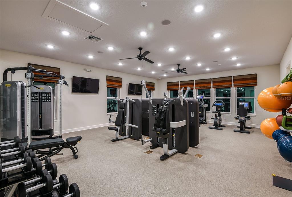 A gym features various strength training machines, a dumbbell rack, exercise balls, and ceiling fans — 7545 LAUREATE BOULEVARD UNIT 7404, ORLANDO, FL