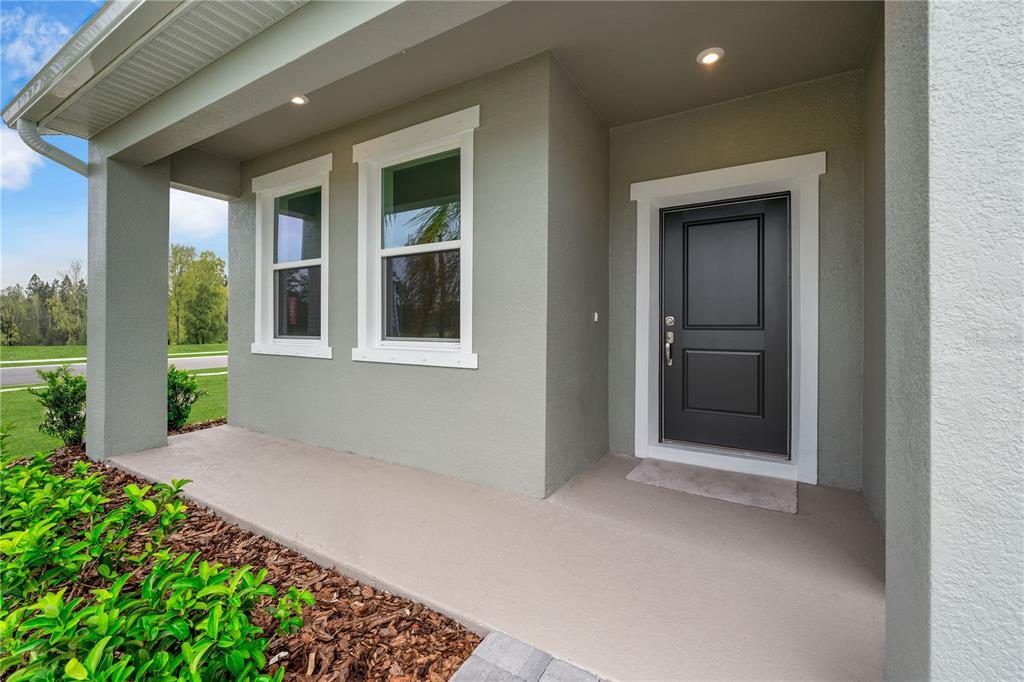 A covered front porch with a black door and two windows on a gray house — 33908 SEATTLE SLEW DRIVE, SORRENTO, FL