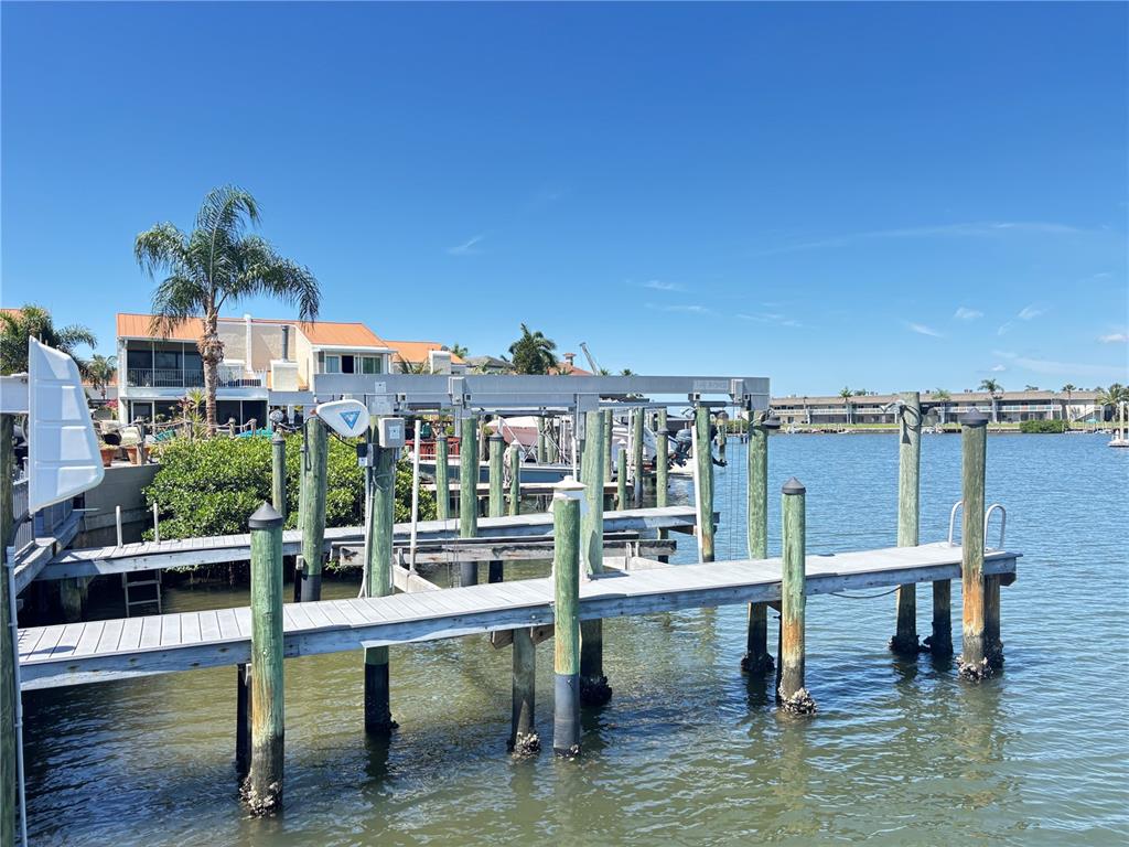 A wooden dock with a boat lift extends into a calm waterway near residential buildings — 4364 OUTRIGGER LANE, TAMPA, FL