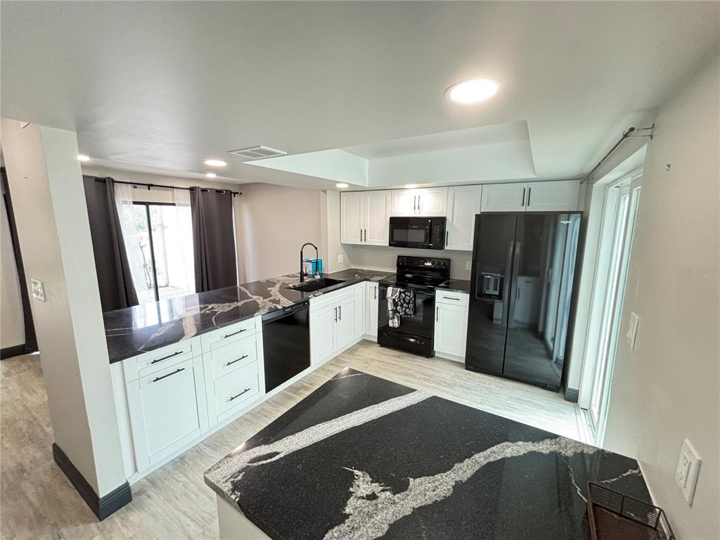 A kitchen features white cabinets, black countertops, and black appliances on light wood-look flooring — 4364 OUTRIGGER LANE, TAMPA, FL