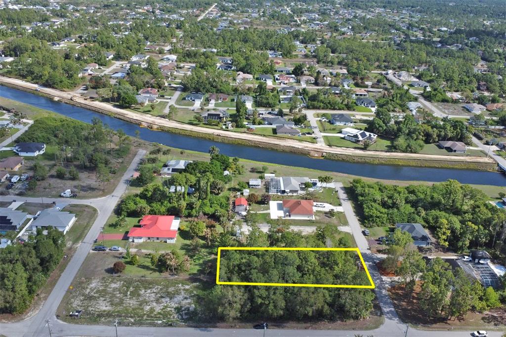 An aerial view shows a rectangular, tree-covered vacant lot outlined in yellow near a canal — 1103 DOROTHY AVENUE N, LEHIGH ACRES, FL