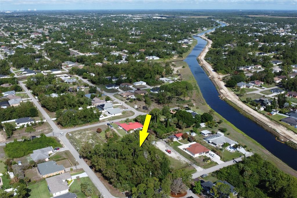 An aerial view shows a wooded vacant lot marked by a yellow arrow near a canal — 1103 DOROTHY AVENUE N, LEHIGH ACRES, FL