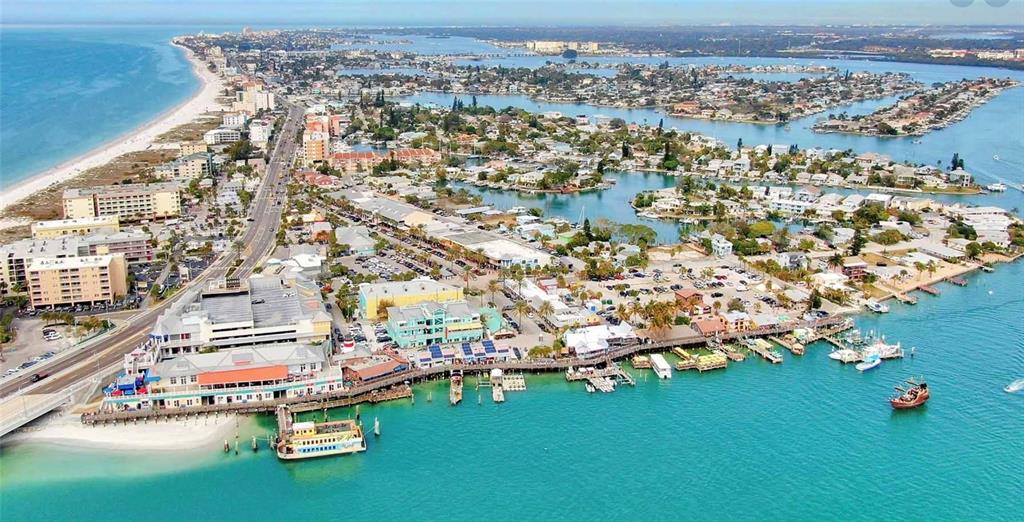 An aerial view shows a coastal town with a beach, marina, and multi-story buildings — 27 DOLPHIN DRIVE, TREASURE ISLAND, FL
