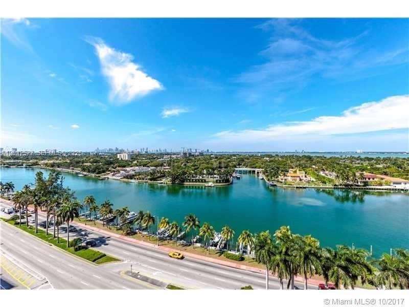 An aerial view shows a coastal road, palm trees, a waterway, and a distant city skyline — 5005 Collins Ave # 1202, Miami Beach FL 33140, MIAMI BEACH, FL