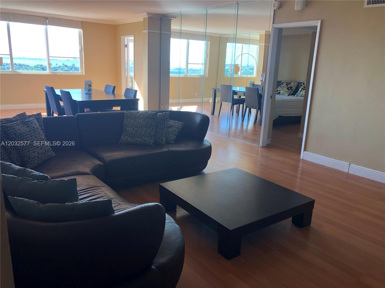 A living room with a dark leather sectional, coffee table, and mirrored wall partition — 5005 Collins Ave # 1202, Miami Beach FL 33140, MIAMI BEACH, FL