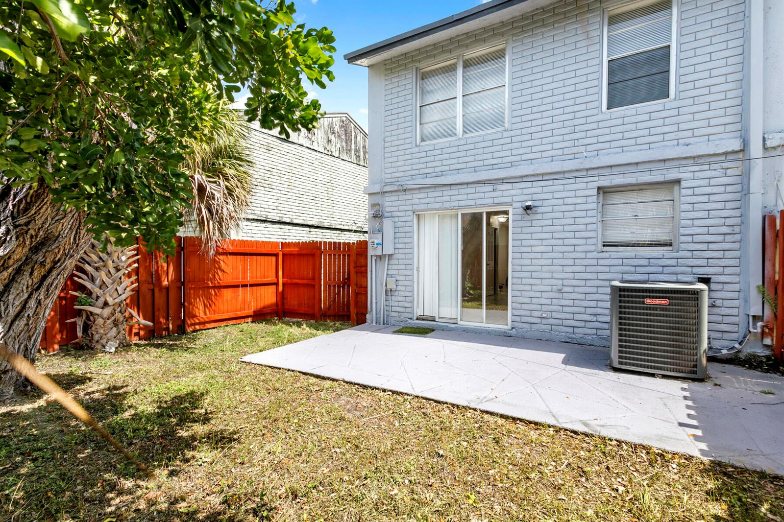 A gray brick two-story house exterior features a concrete patio, sliding glass doors, and AC unit — RIVIERA BEACH, FL