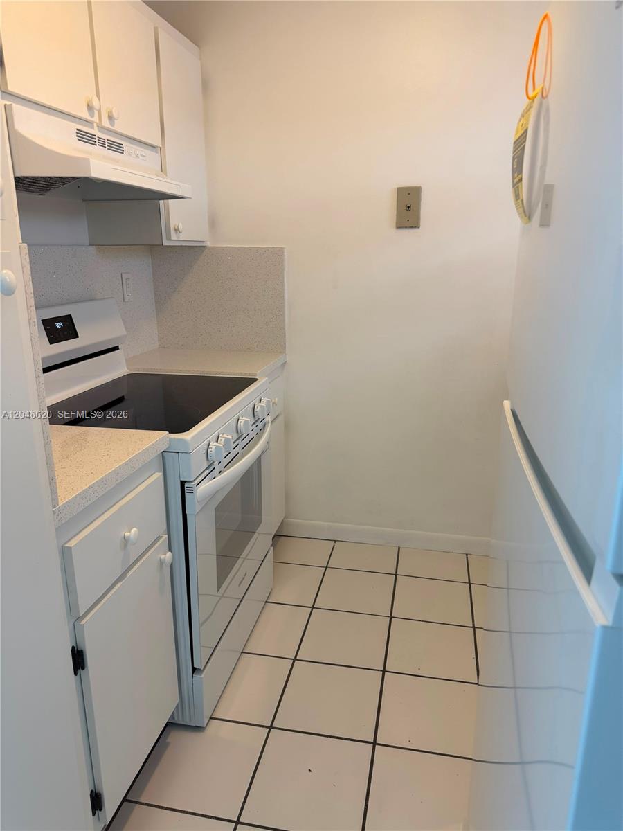 A narrow kitchen features white cabinets, a white electric stove, and light-colored tiled flooring — 600 NW 32nd Pl # 312, Miami FL 33125, MIAMI, FL
