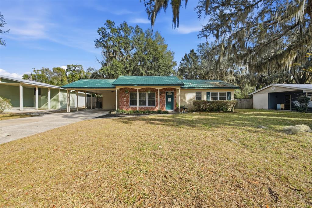 A single-story house with a green metal roof, brick accents, and a large attached carport — 133 CRESTWOOD AVENUE, PALATKA, FL