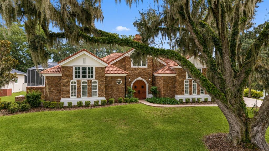 A stone-clad house with a red tile roof sits behind a large mossy oak tree — 1718 SW 27TH STREET, OCALA, FL