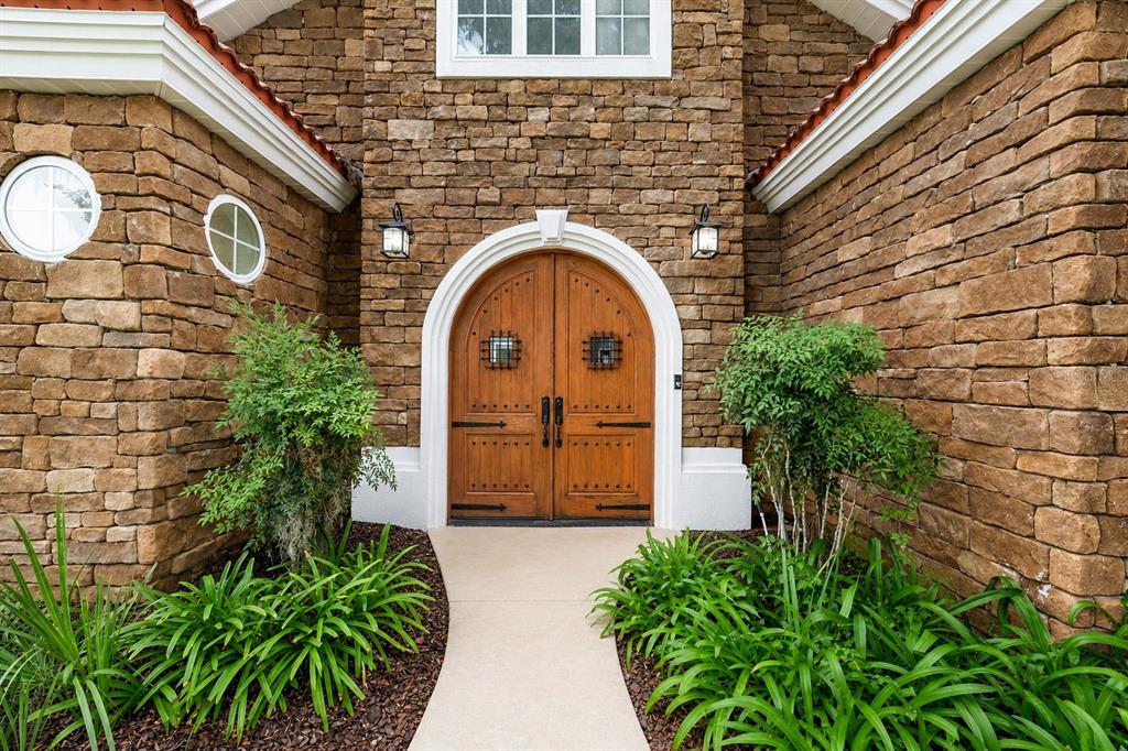An arched wooden double door serves as the entrance to a stone-clad home exterior — 1718 SW 27TH STREET, OCALA, FL