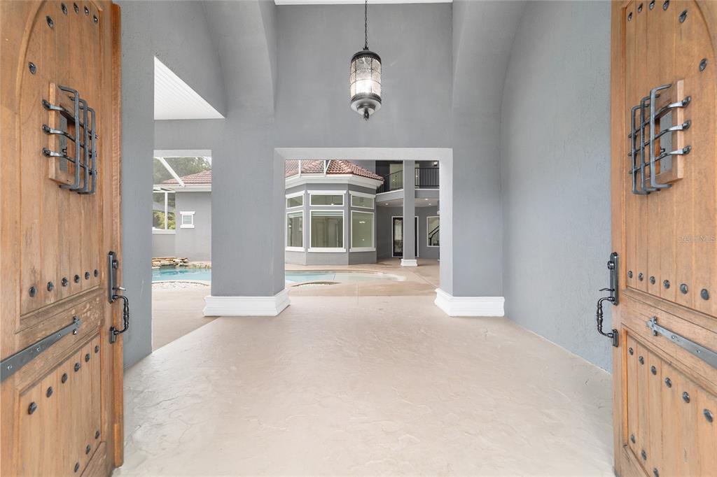 A view through open wooden doors into a covered entryway looking out toward a pool — 1718 SW 27TH STREET, OCALA, FL