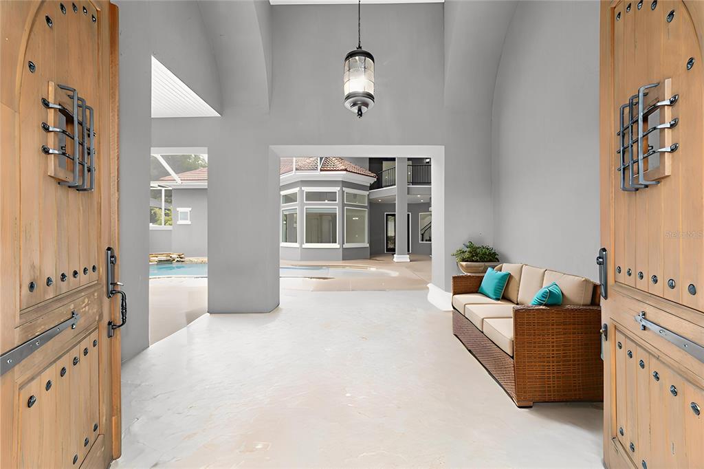 An open-air entryway features double wooden doors, a wicker sofa, and a view of a pool — 1718 SW 27TH STREET, OCALA, FL