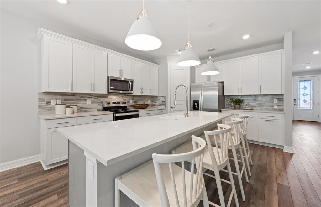 A modern kitchen features white cabinetry, a large island with bar stools, and stainless appliances — 7465 SUMMER COURT, SARASOTA, FL