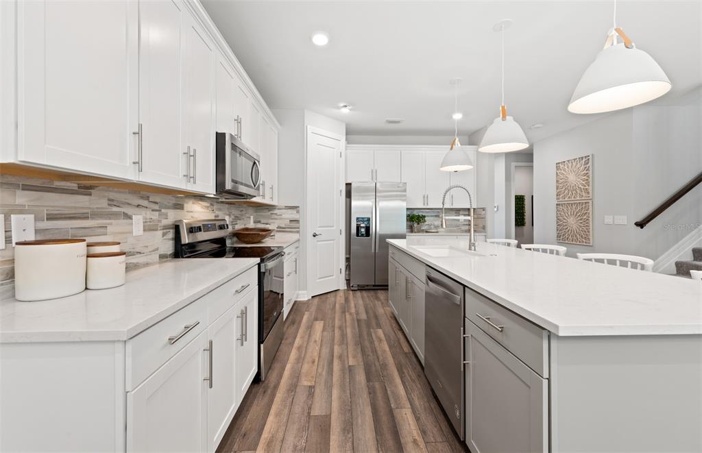 A modern kitchen features white cabinetry, a gray island, stainless steel appliances, and wood flooring — 7465 SUMMER COURT, SARASOTA, FL