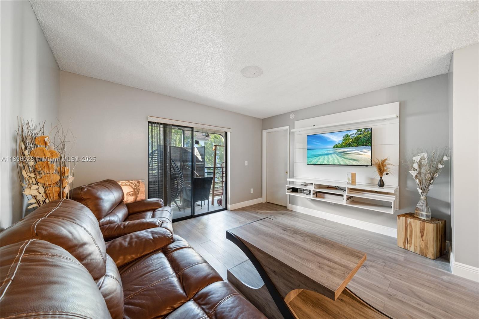 A living room features a brown leather sofa, wood-look flooring, and a wall-mounted television unit — 861 NE 207th Ln # 14, Miami FL 33179, MIAMI, FL