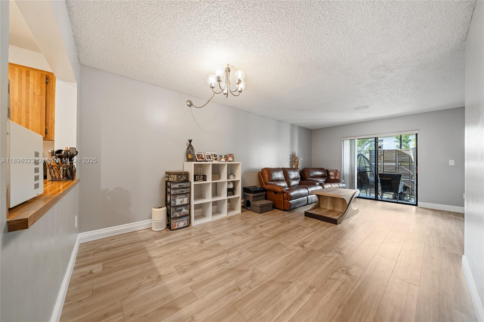 A living room features light wood-look flooring, gray walls, a leather sofa, and sliding glass doors — 861 NE 207th Ln # 14, Miami FL 33179, MIAMI, FL