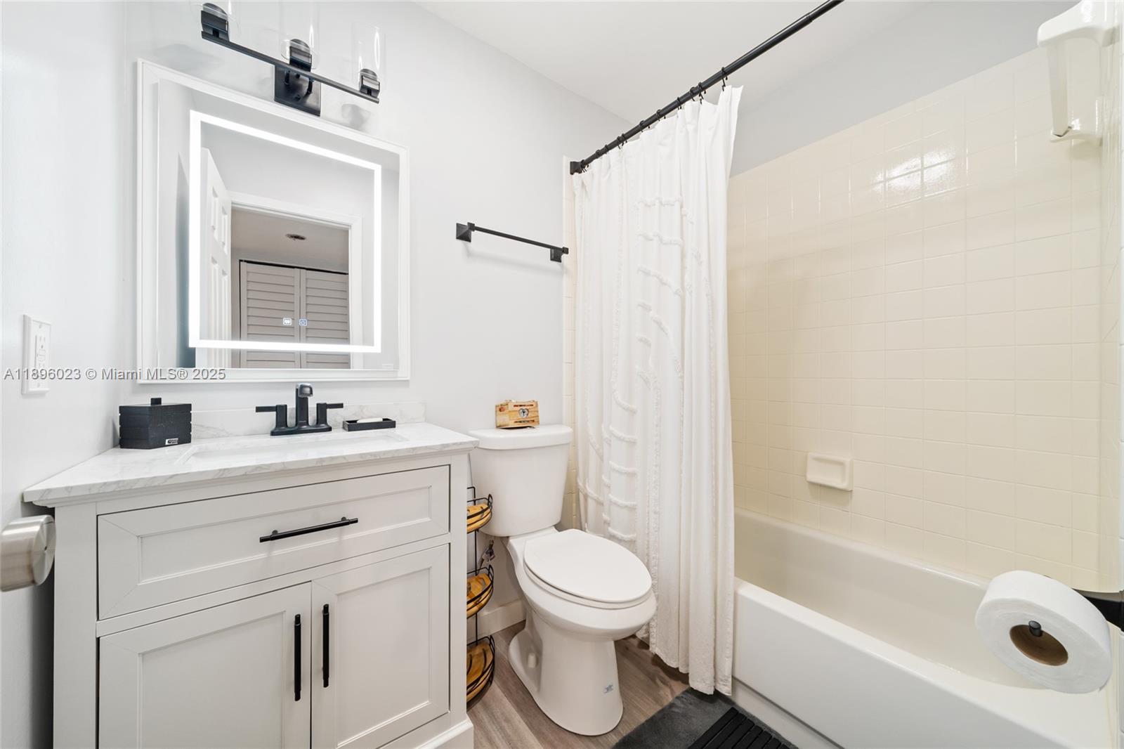A bathroom features a white vanity, a lighted mirror, a toilet, and a shower-tub combo — 861 NE 207th Ln # 14, Miami FL 33179, MIAMI, FL