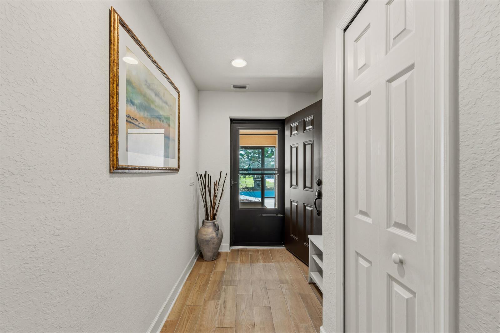 A bright entryway features wood-look tile flooring, a dark front door, and a framed painting — 6700 Dulce Real Avenue, Fort Pierce FL 34951, FORT PIERCE, FL
