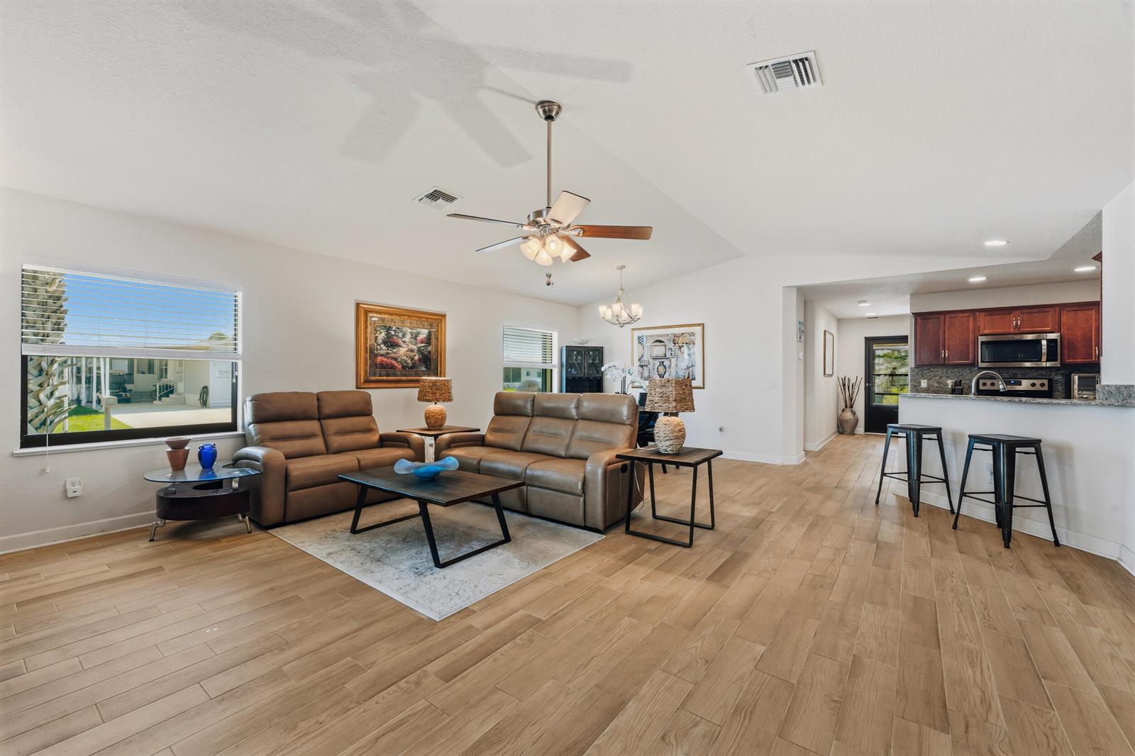 A living room with light wood floors, brown leather sofas, and an open kitchen area — 6700 Dulce Real Avenue, Fort Pierce FL 34951, FORT PIERCE, FL