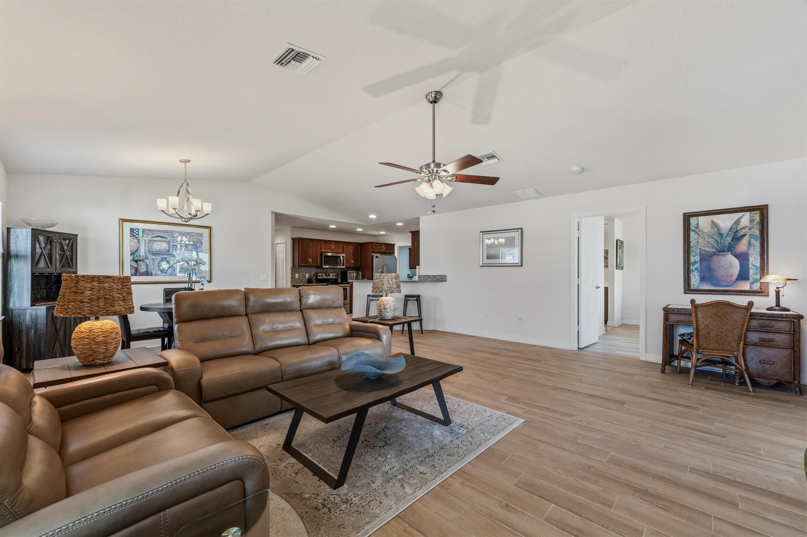 A living room features light wood-look tile flooring, leather furniture, and an open kitchen area — 6700 Dulce Real Avenue, Fort Pierce FL 34951, FORT PIERCE, FL