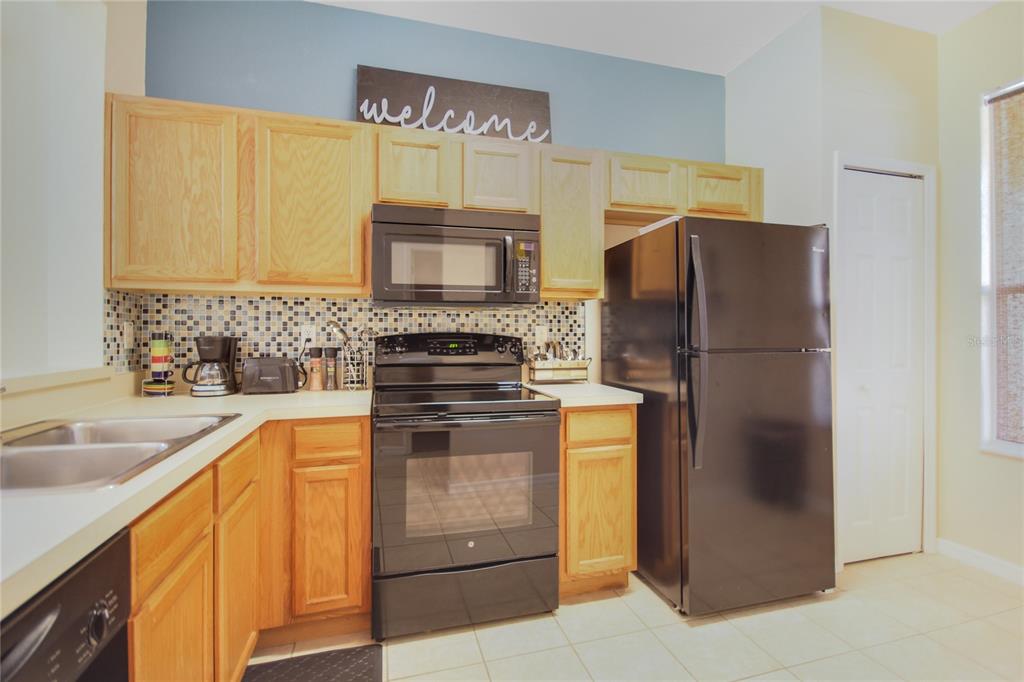 A kitchen features light wood cabinets, black appliances, a mosaic tile backsplash, and tile flooring — 2740 COUPE STREET, KISSIMMEE, FL