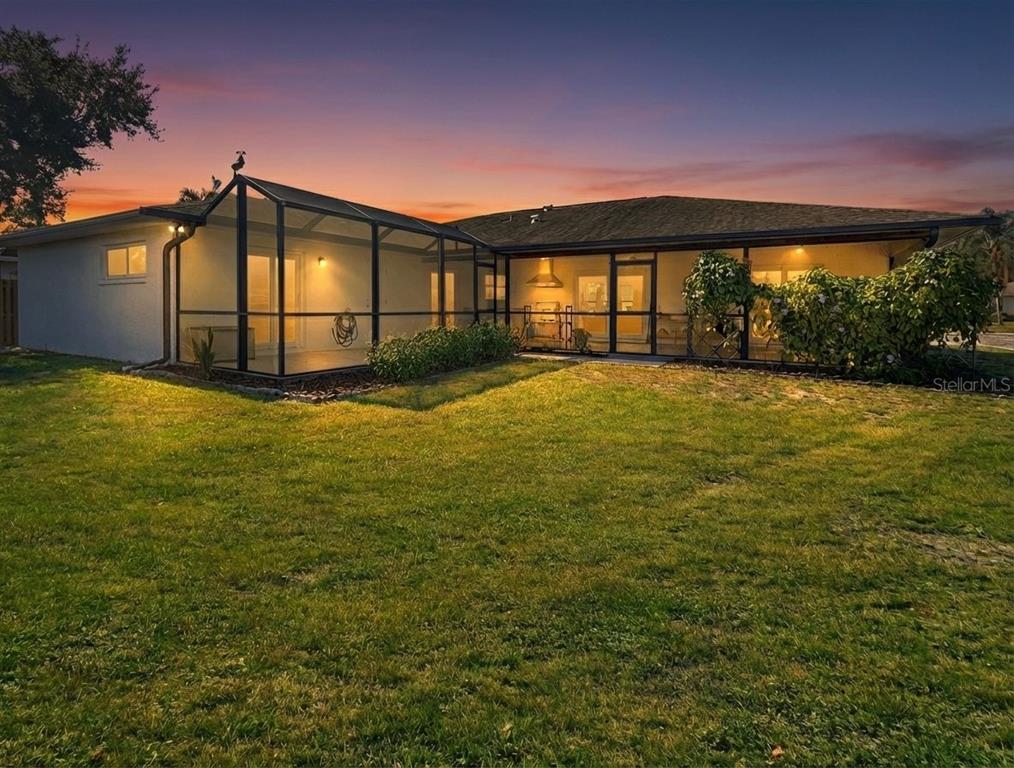 The rear exterior of a house features a screened-in patio and a large grassy yard — 2042 COUNTRY MEADOWS PLACE, SARASOTA, FL