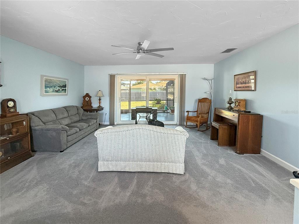 A living room features gray carpet, light blue walls, a ceiling fan, and sliding glass doors — 2042 COUNTRY MEADOWS PLACE, SARASOTA, FL