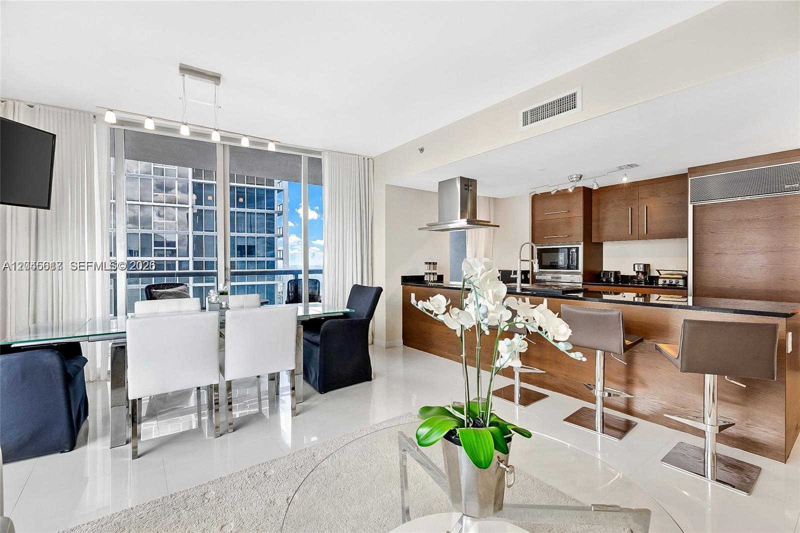 A modern open-concept kitchen and dining area features white tile floors and balcony views — 485 Brickell Ave # 3602, Miami FL 33131, MIAMI, FL