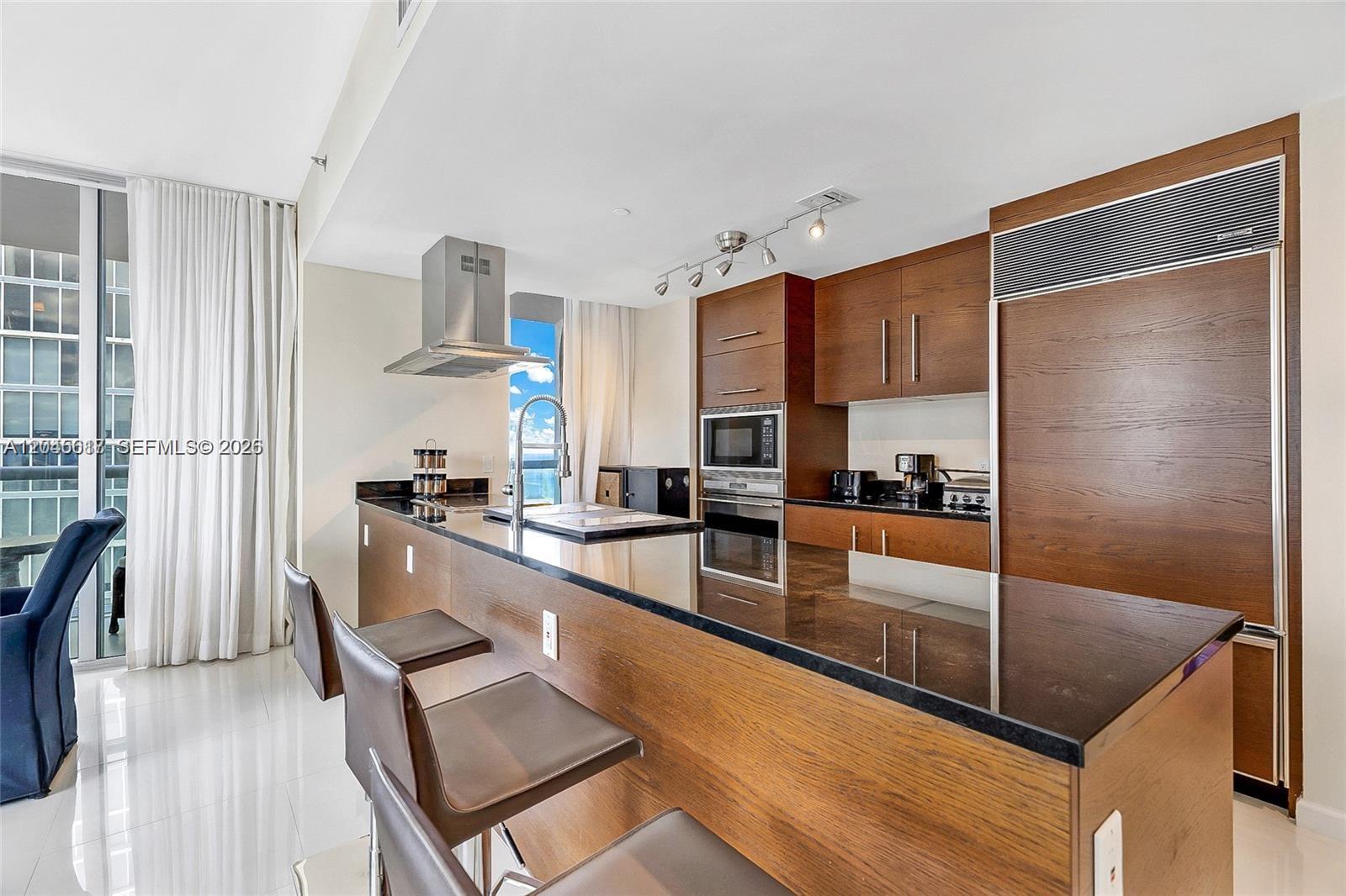 A modern kitchen features dark wood cabinetry, black granite countertops, and a breakfast bar — 485 Brickell Ave # 3602, Miami FL 33131, MIAMI, FL