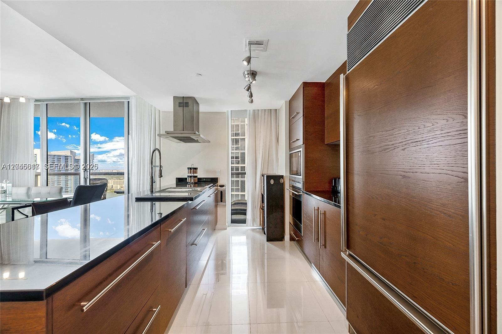 A modern kitchen features dark wood cabinetry, black countertops, stainless steel appliances, and tile flooring — 485 Brickell Ave # 3602, Miami FL 33131, MIAMI, FL