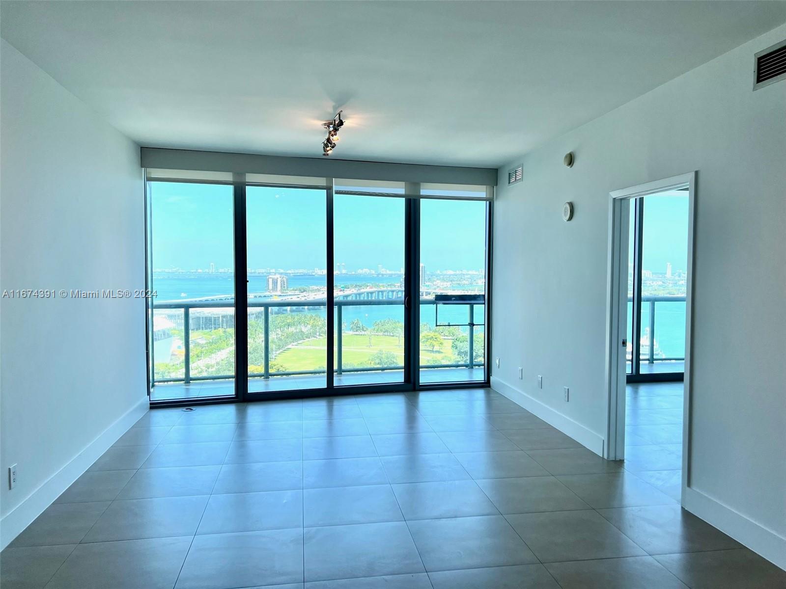 An empty room with tile floors features floor-to-ceiling windows overlooking a bay and park — 888 Biscayne Blvd # 1811, Miami FL 33132, MIAMI, FL