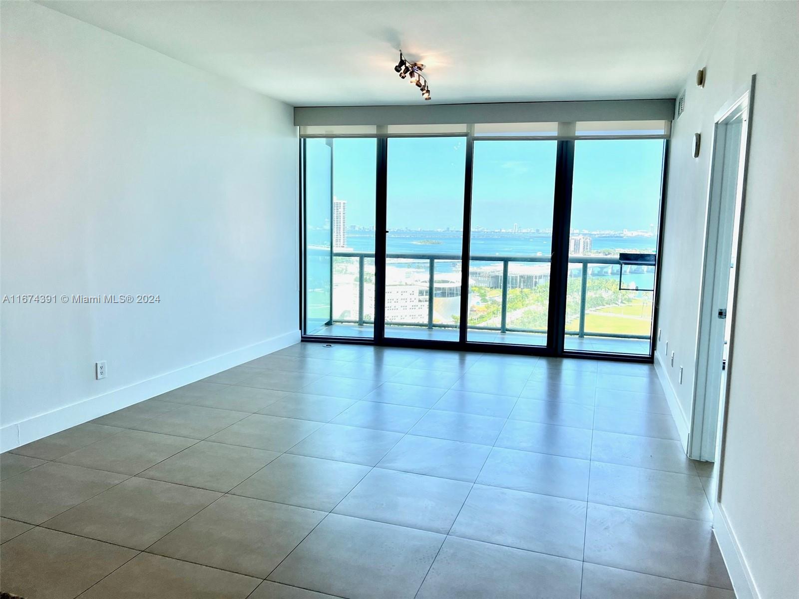 An empty room features large floor-to-ceiling windows with a water view and tiled flooring — 888 Biscayne Blvd # 1811, Miami FL 33132, MIAMI, FL