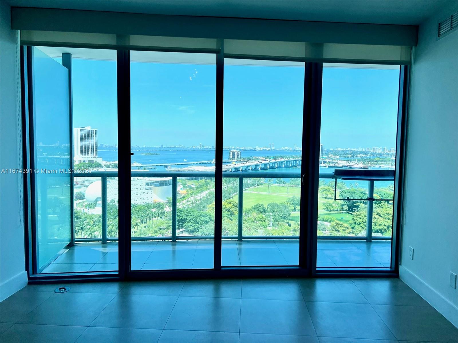 A room with large floor-to-ceiling windows overlooking a bay, a bridge, and a park — 888 Biscayne Blvd # 1811, Miami FL 33132, MIAMI, FL