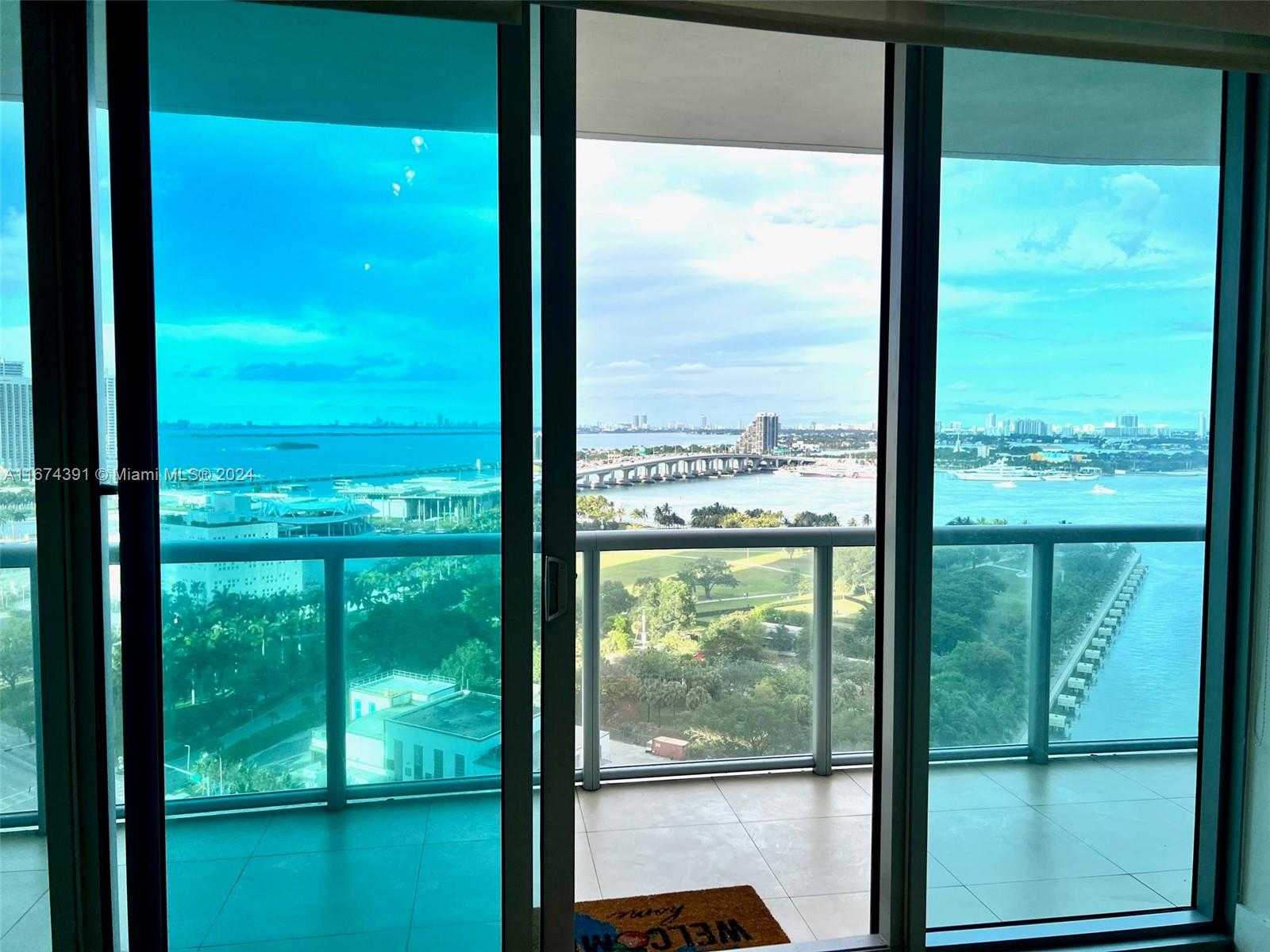 A balcony with a glass railing overlooks a bay, a bridge, and a city skyline — 888 Biscayne Blvd # 1811, Miami FL 33132, MIAMI, FL