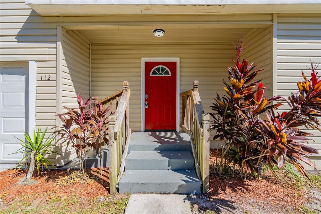The exterior of a home features a red front door, concrete steps, and wooden railings — 112 S MOSS STREET, LEESBURG, FL