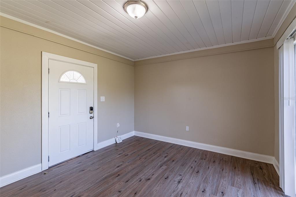 An empty room features wood-look flooring, beige walls, a white door, and a paneled ceiling — 112 S MOSS STREET, LEESBURG, FL