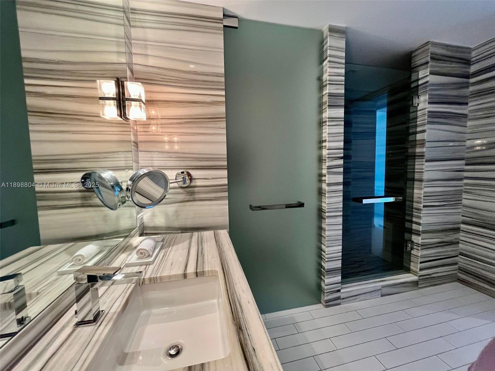A modern bathroom features a marble vanity, a glass-enclosed shower, and a frosted glass door — 2201 Collins Ave # 626, Miami Beach FL 33139, MIAMI BEACH, FL