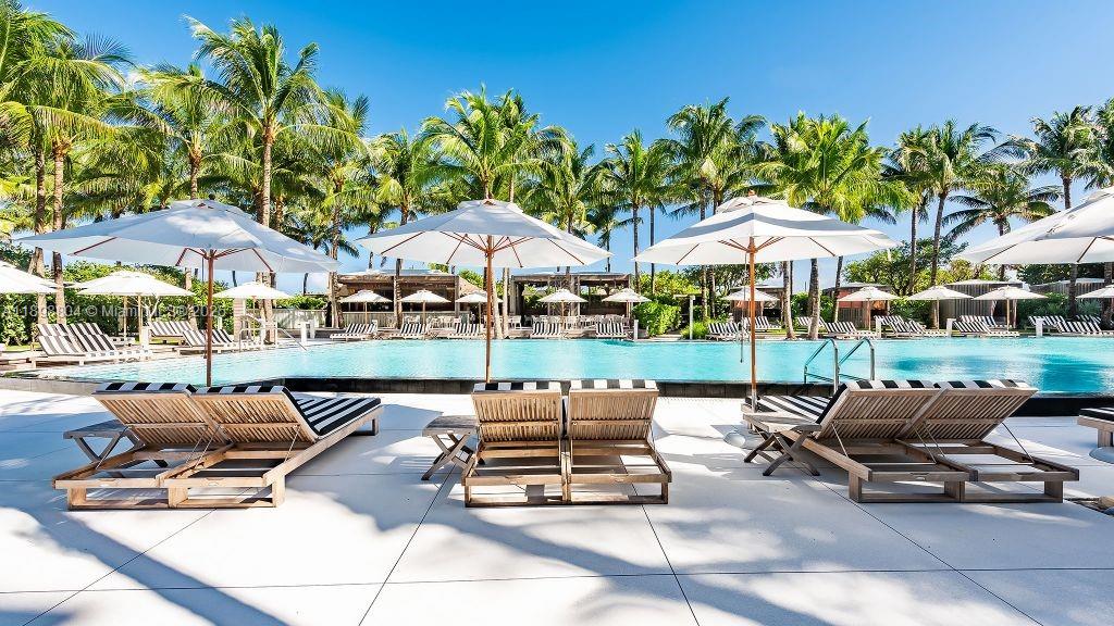 A swimming pool is surrounded by lounge chairs, white umbrellas, and palm trees — 2201 Collins Ave # 626, Miami Beach FL 33139, MIAMI BEACH, FL