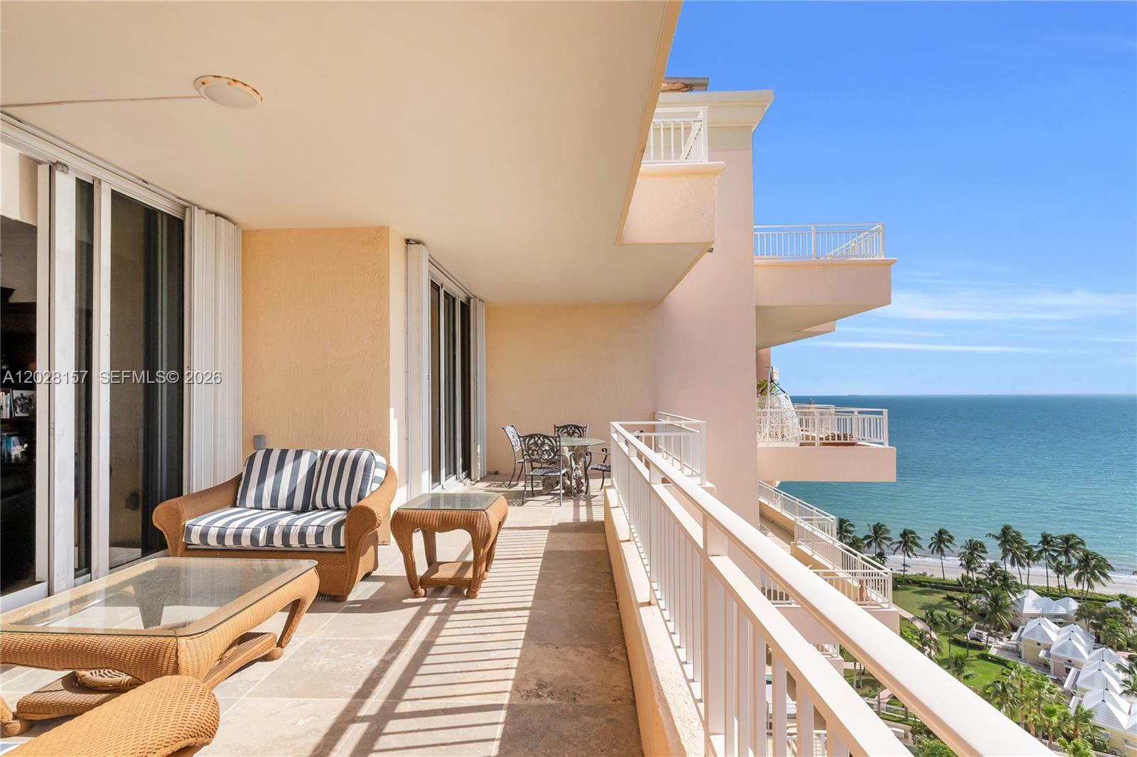 A balcony with wicker furniture overlooks the ocean and palm trees from a high floor — 791 Crandon Blvd, Key Biscayne FL 33149, KEY BISCAYNE, FL