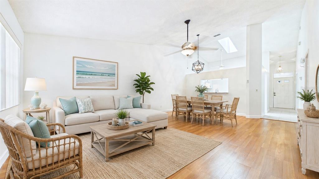 A living and dining area features light wood flooring, a beige sectional, and rattan furniture — 1539 REBECCA LANE, DUNEDIN, FL