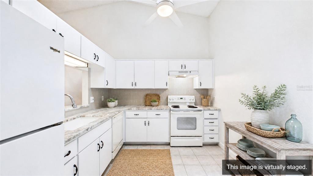 A bright kitchen features white cabinets, white appliances, and a light-colored countertop — 1539 REBECCA LANE, DUNEDIN, FL