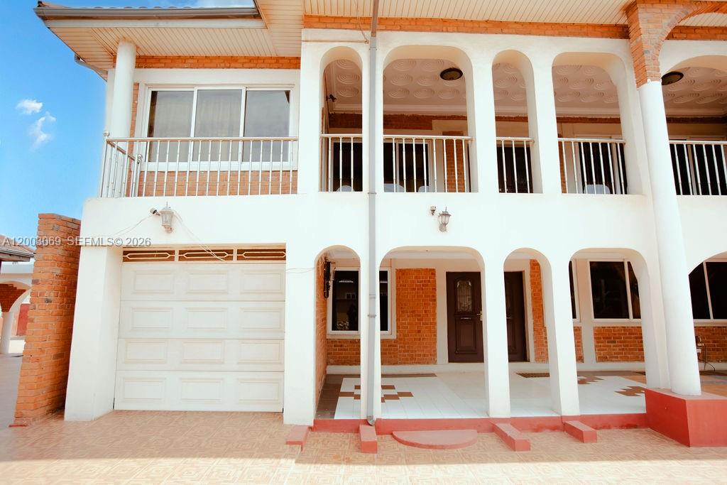 A two-story house features a white facade, arched entryways, a garage, and a balcony — 72 Nmai Dzorn Adjiringano Road, FL