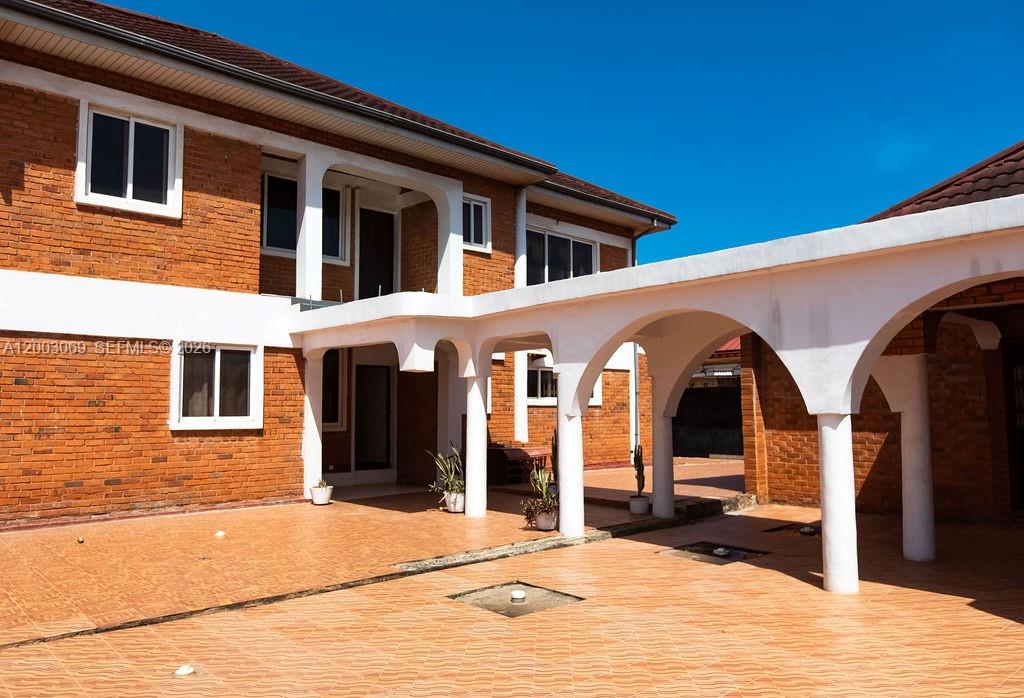 A two-story brick house features a covered patio with white arched columns and tile flooring — 72 Nmai Dzorn Adjiringano Road, FL